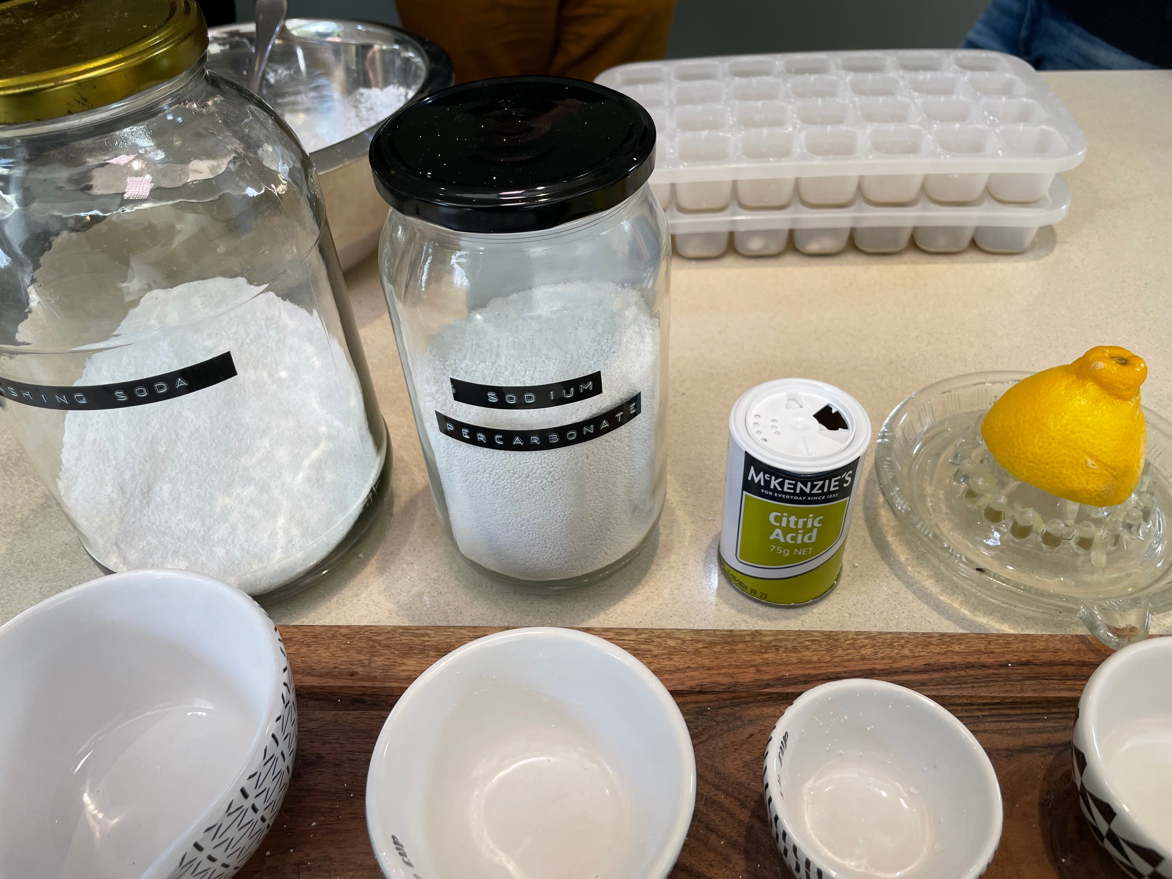 Two jars of white powder, a small white container and a lemon on a squeezer on