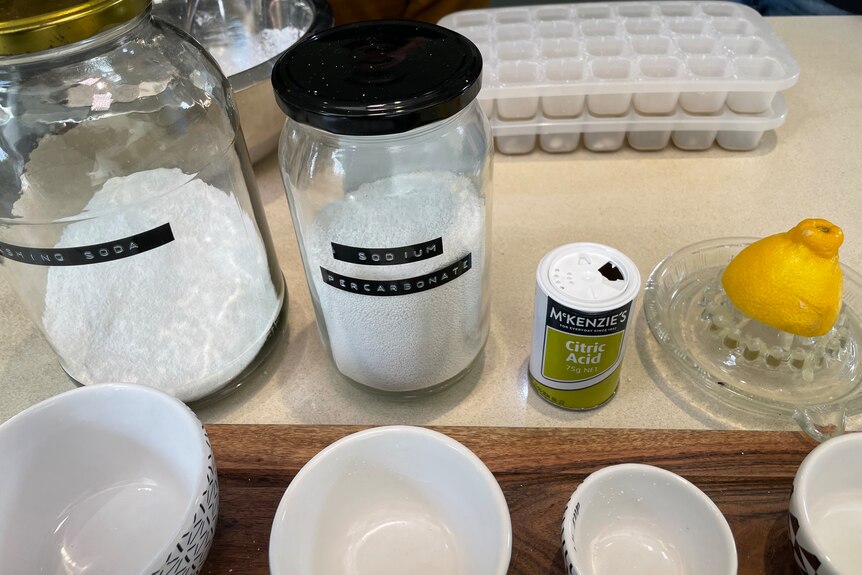 Two jars of white powder, a small white container and a lemon on a squeezer on