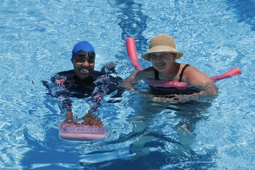 Two women swim with flotation devices in an outdoor pool.