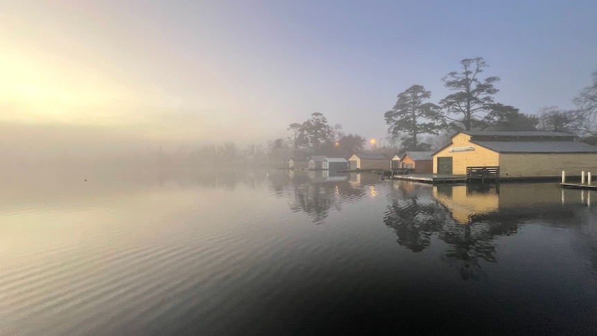 Sunrise above a rowing boatshed beside a still lake