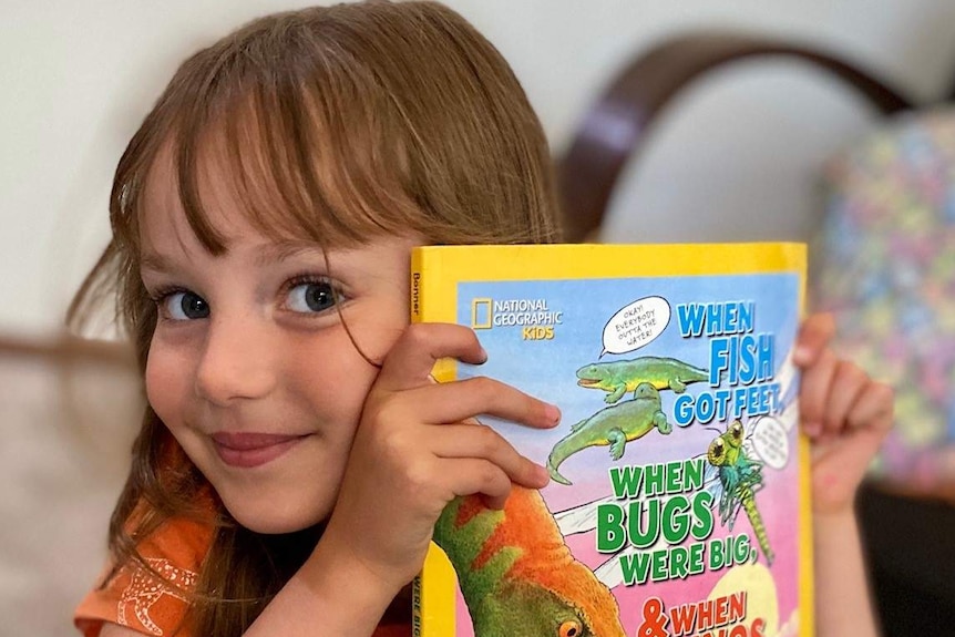 A girl in an orange t-shirt holds up a National Geographic Kids magazine