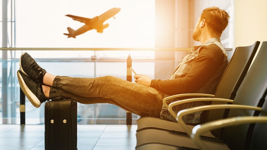 A man sits in an airport departure lounge watching a plane take off.