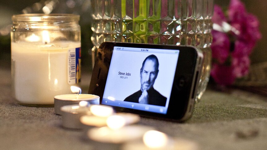 Candles, flowers, and an iPhone with Steve Jobs photo displayed, are seen in remembrance of the Apple visionary.