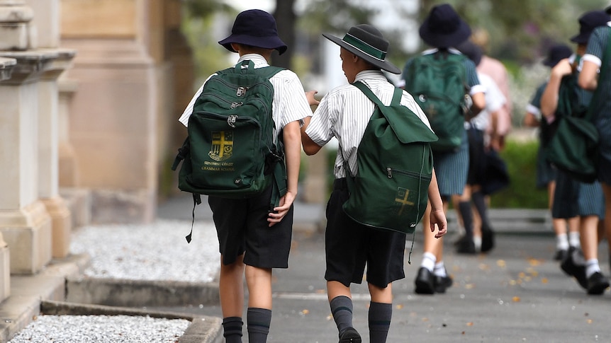 Two boys with long songs and oversized backpacks chat and walk