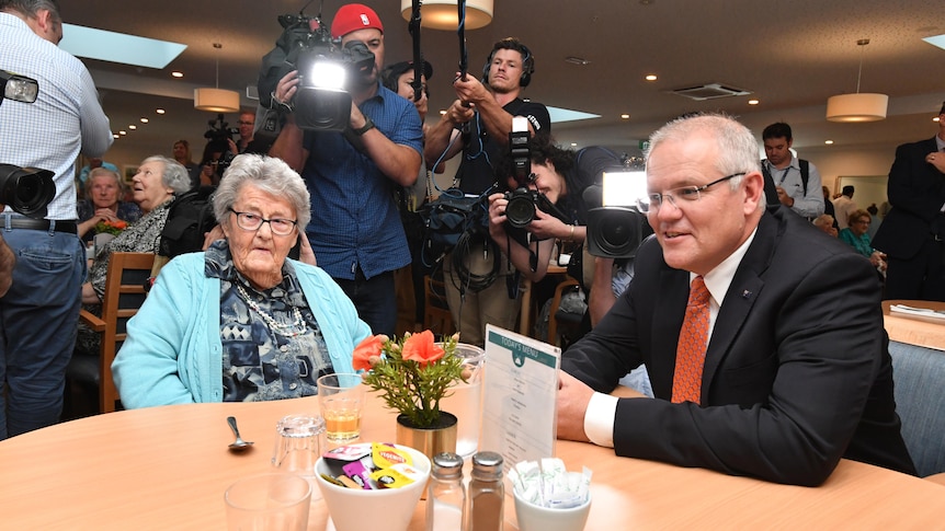 Scott Morrison sits down with a woman in a nursing home surrounded by cameras.