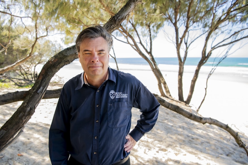 A man in a Bond University shirt standing on the beach.