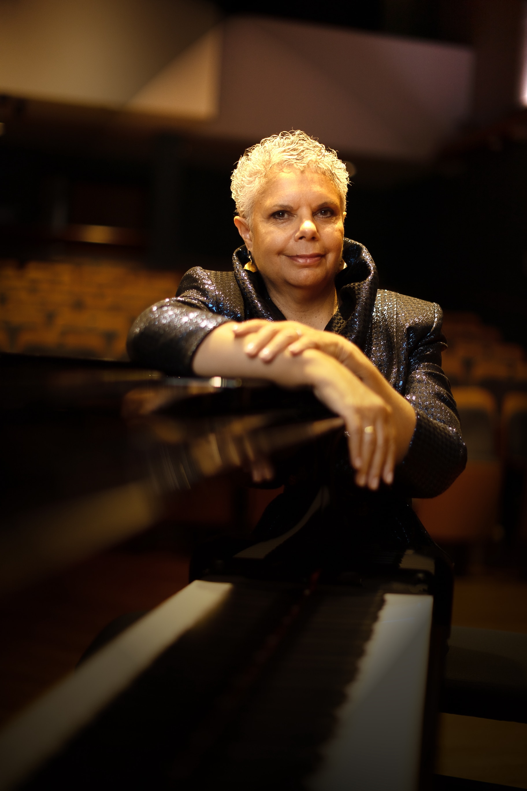 Deborah Cheetham Fraillon stands behind a piano in the Sydney Conservatorium of Music's Verbrugghen Hall