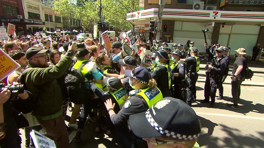 a line of police clash with protesters who appear to crash into them in the street.