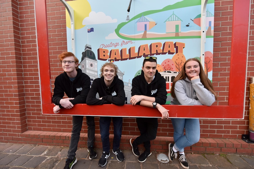Four young people stand inside a mounted picture frame. A mural saying 'Greetings from Ballarat' is in the background.
