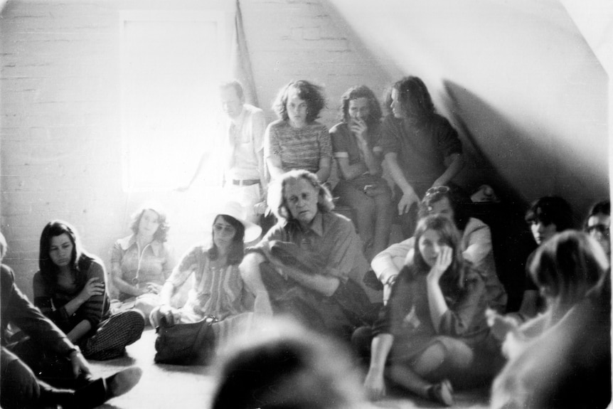 A group of young people having a discussion in an empty room with some people sitting on the floor.