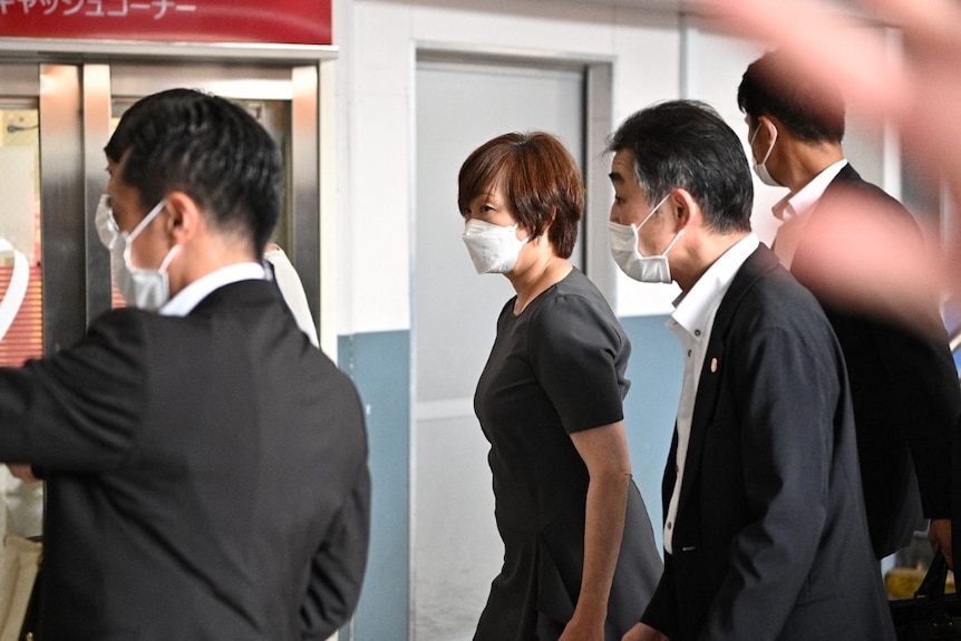 Akie Abe walking with men in suits and face masks