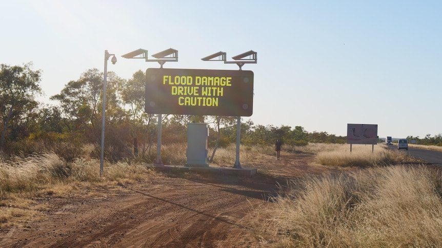 On the left hand side of a highway is a big electric sign with yellow words reading "flood damage drive with caution".