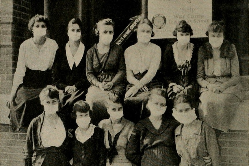 A black and white photo showing a group of women wearing face masks in front of a brick wall.