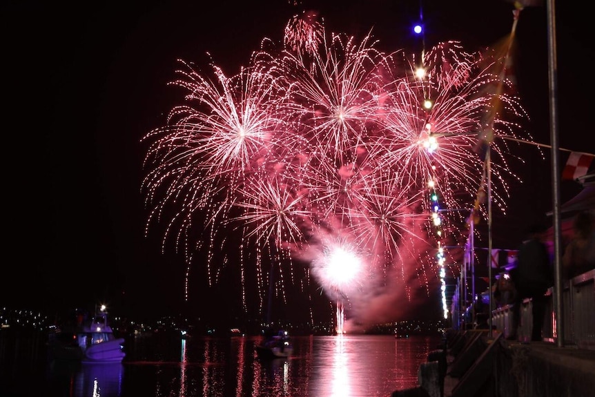 Bright red fireworks light up the dark night sky over water.