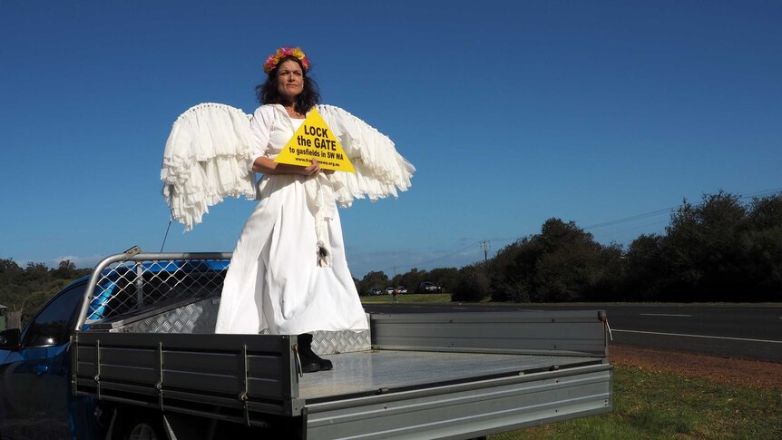 A woman dressed as an angel stands in the back of a flat-bed truck holding a sign saying 'lock the gate'.