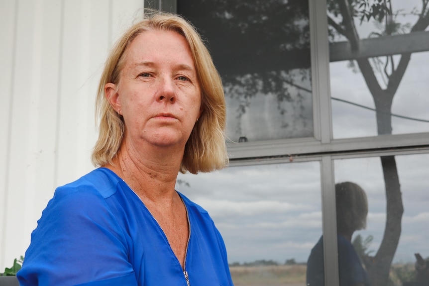 A woman sitting outside a house looking at the camera with a neutral expression.