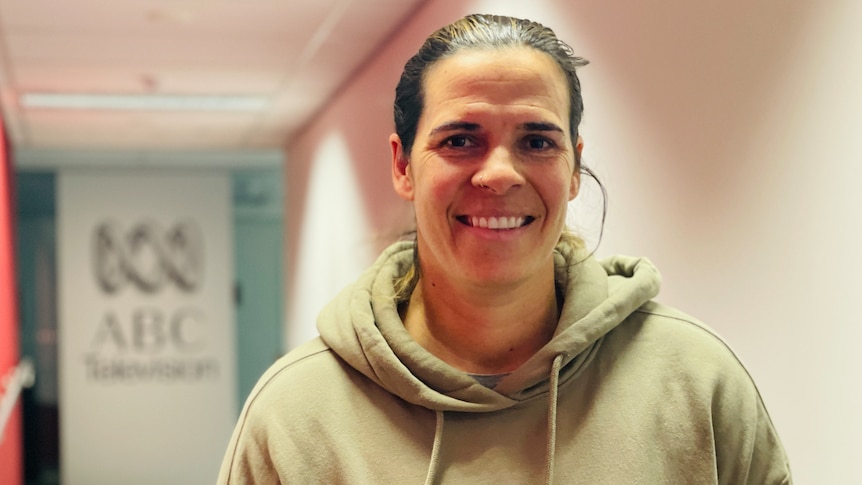 woman stands in a corridor smiling in a beige hoodie