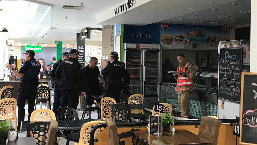 Police and a firefighter stand among tables and chairs at a cafe.