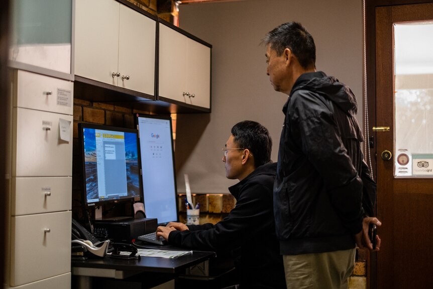 Jason Zhou works on the computer while his father looks over his shoulder. 