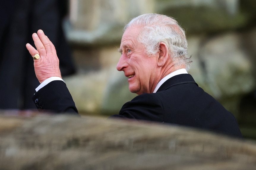 King Charles waves a hand with one gold ring on his pinky finger