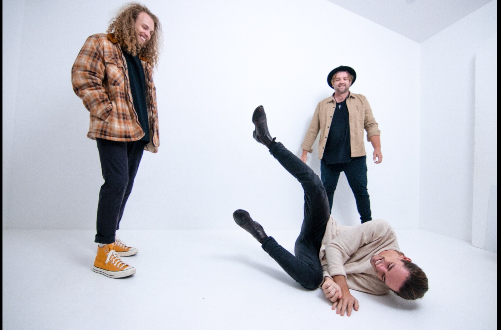 three band members laugh and joke around in front of a white studio background
