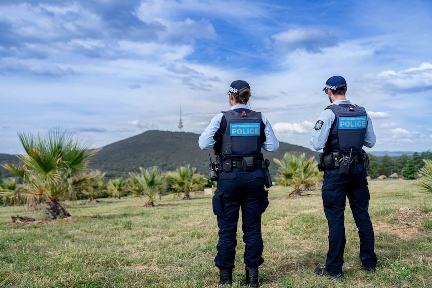 The backs of two police officers who are looking at a mountain in the background. 