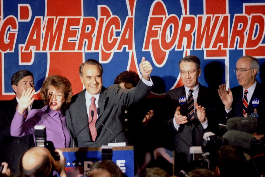 Bob Dole and his wife Elizabeth on stage with a big sign behind them. 