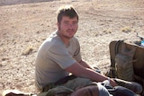 A man in the Australian Army sits in a sunny field in the outback desert.