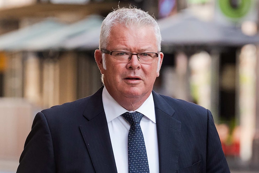 A mid-shot of former WA treasurer Troy Buswell walking outside Perth's Central Law Courts wearing a suit and tie.