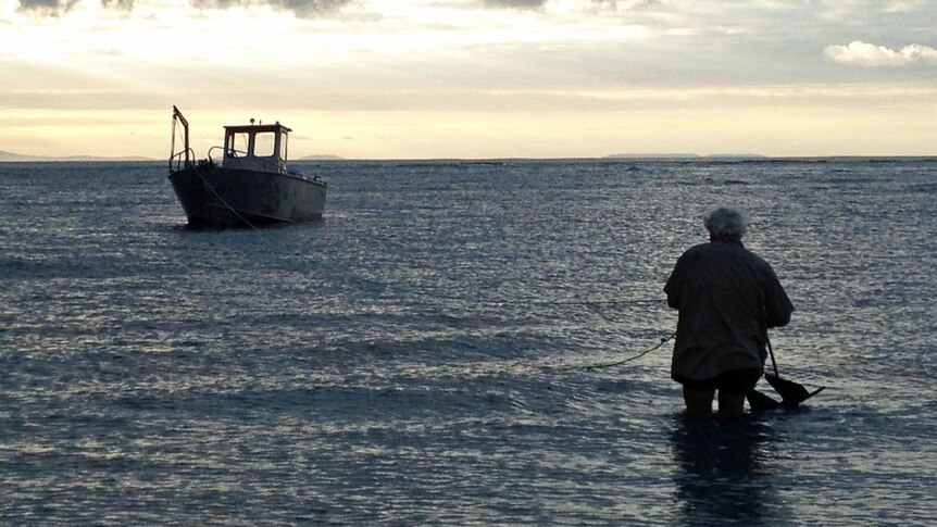Michael Mansell knee deep in water hauling in a 5 metre aluminium boat as sunset