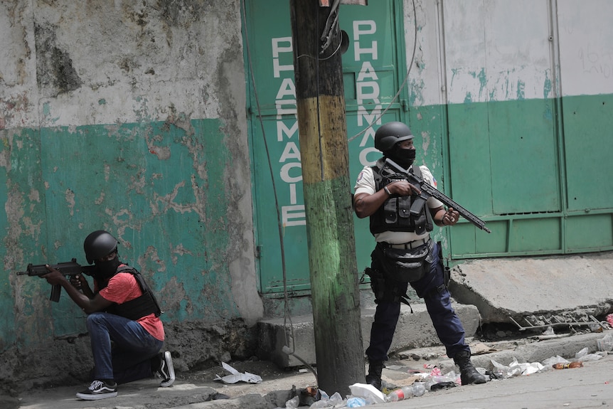 Two men wearing body armour and carrying weapons patrol a street 