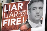 A poster displaying Michael Cohen's face alongside the words 'LIAR, LIAR, PANTS ON FIRE' is displayed during a public hearing.