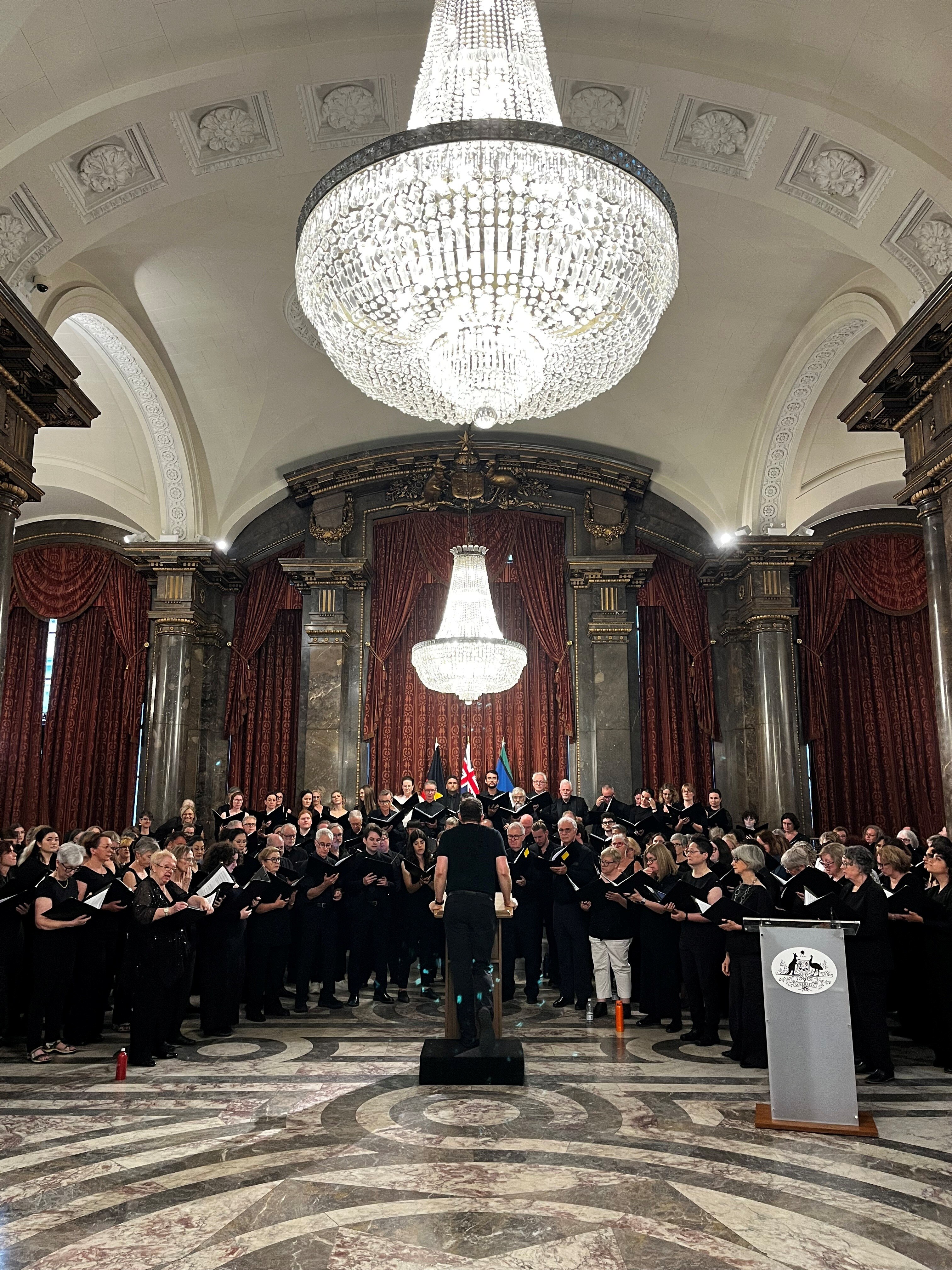 Sydney Philharmonia performing in the Australia House in London. The ornate hall features huge chandeliers and gilded columns.