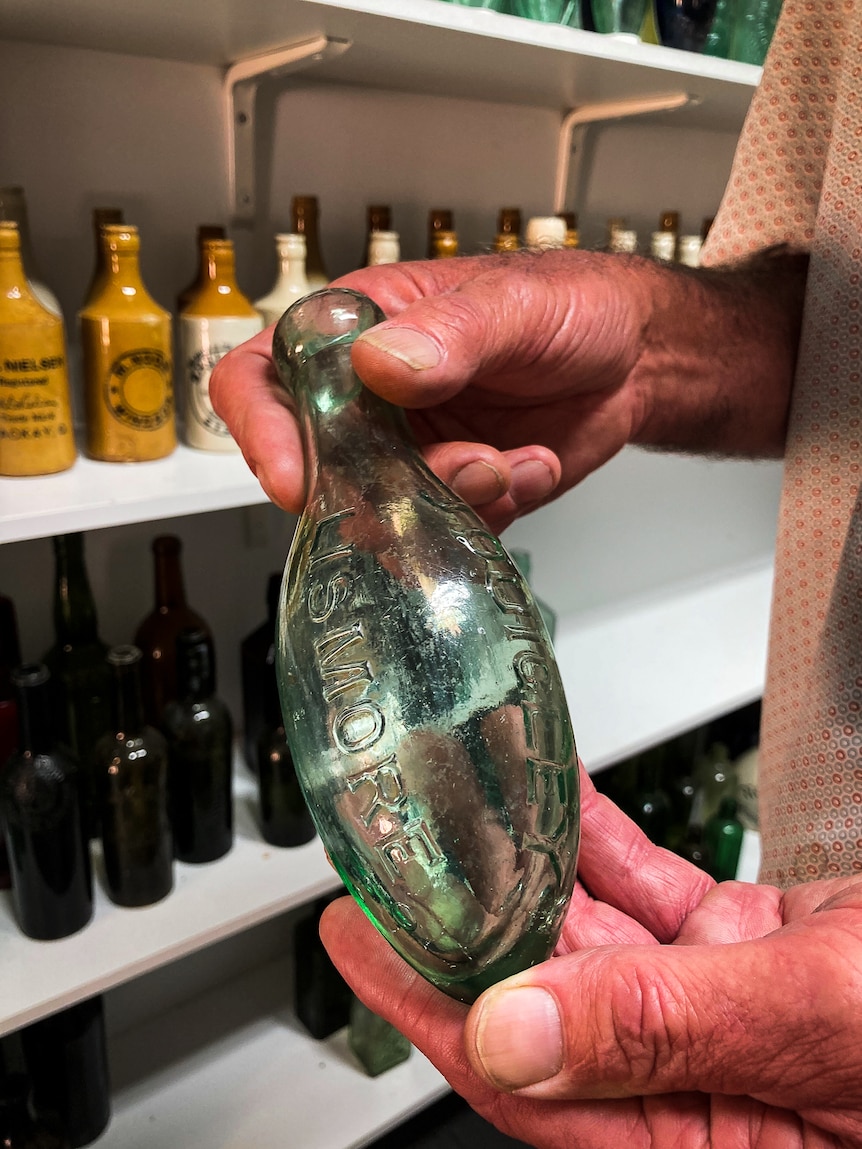 Man holding clear glass bottle with a egg shaped bottom and flask shaped top.