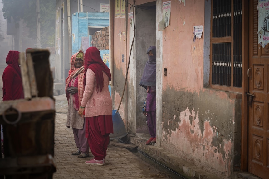 A group of women in maroon robes stand outside a doorway