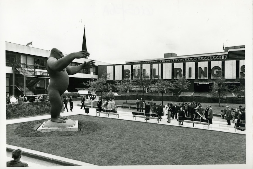 Una foto en blanco y negro de una enorme estatua de King Kong, con 'Plaza de toros' escrito en un edificio cercano