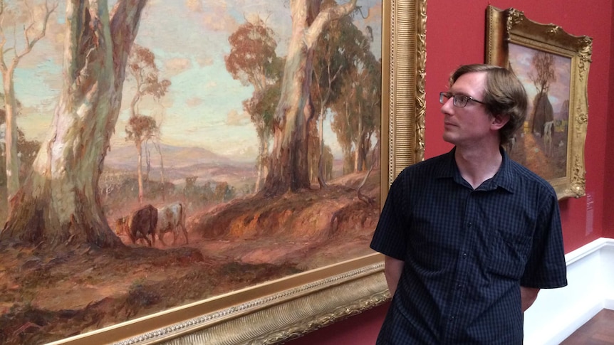 Art history student Ralph Body looks at a hanging Sir Hans Heysen painting.
