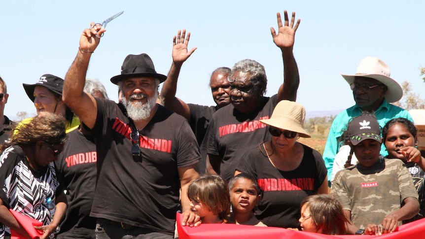 A group of people wave their hands in the air after cutting a red ribbon on a remote highway