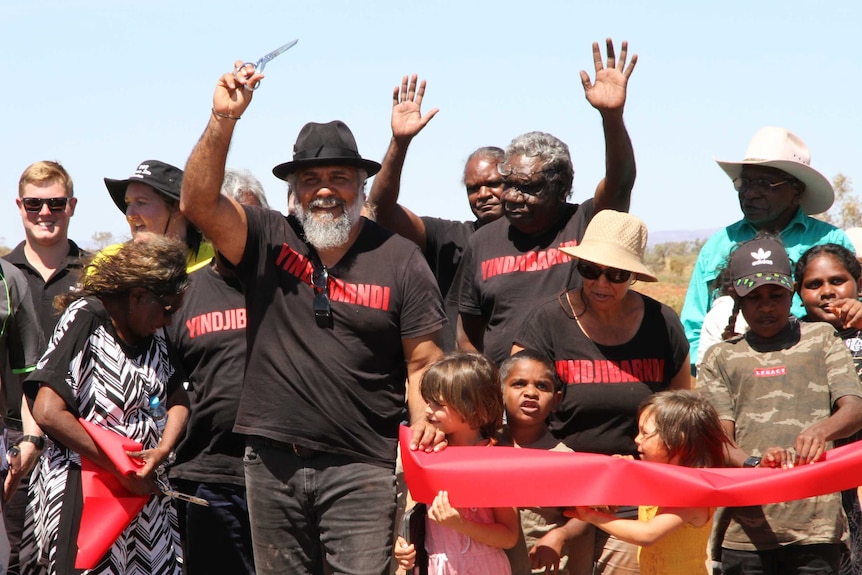 A group of people wave their hands in the air after cutting a red ribbon on a remote highway