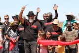 A group of people wave their hands in the air after cutting a red ribbon on a remote highway