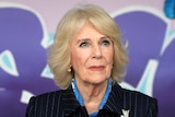 Camilla looks overhead, standing in front of a wall painted in pastel colours