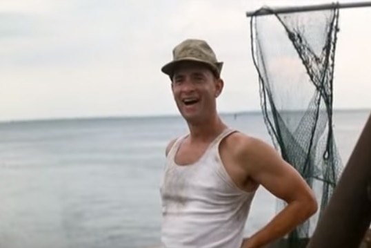 Tom Hanks in the character of Forrest Gump stands on a boat.