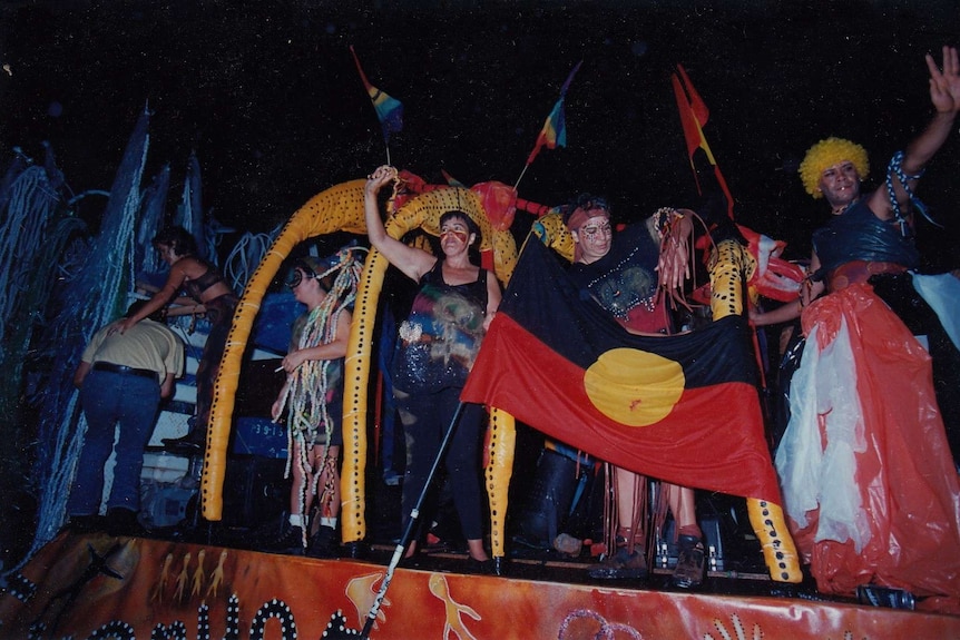 People dressed in black, red and yellow, with Aboriginal flags, wave from Mardi Gras float.