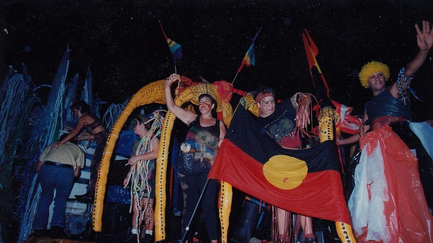 People dressed in black, red and yellow, with Aboriginal flags, wave from Mardi Gras float.