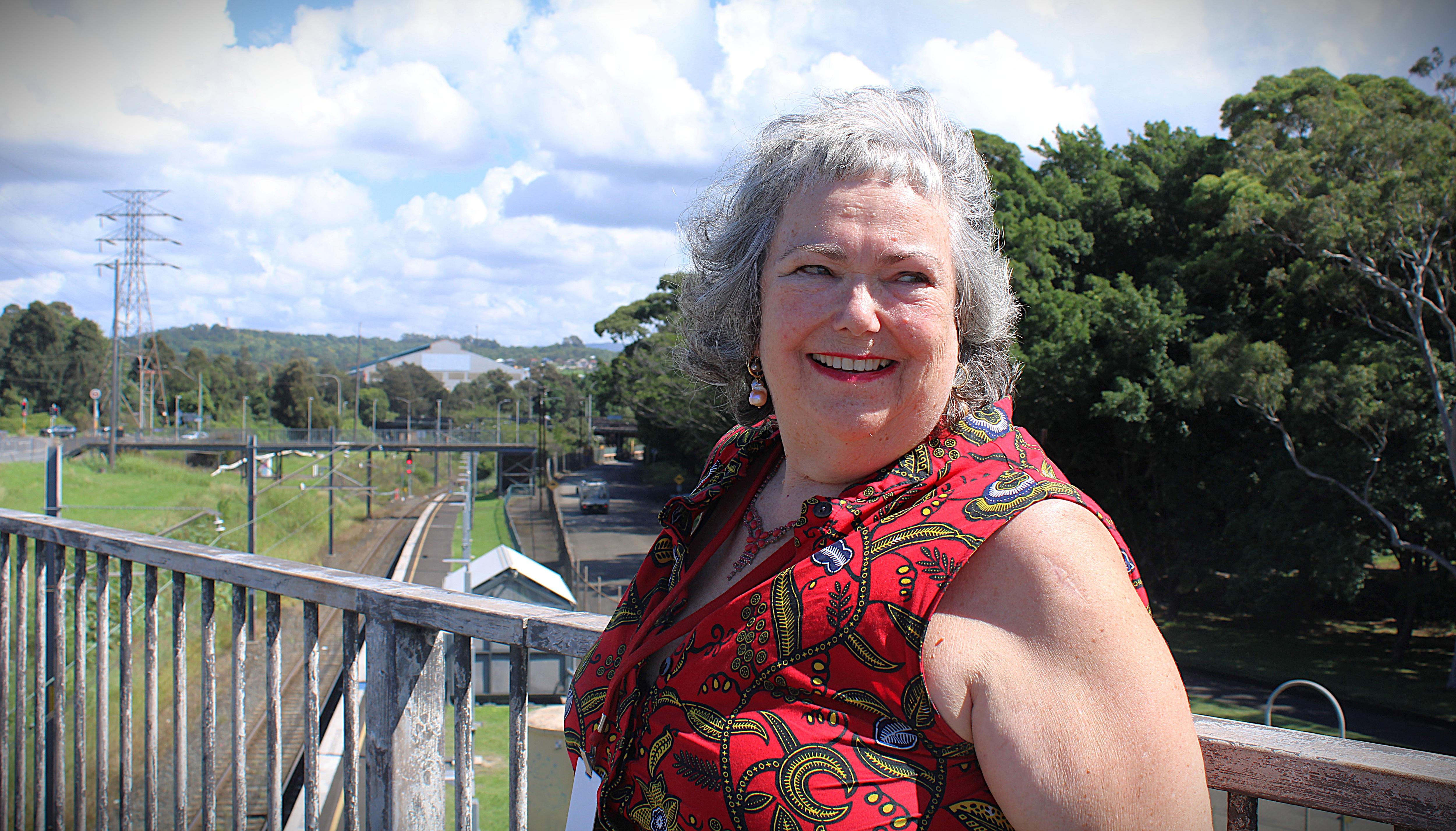 Mujer con pelo gris y ropa roja sonríe cerca de un sitio industrial