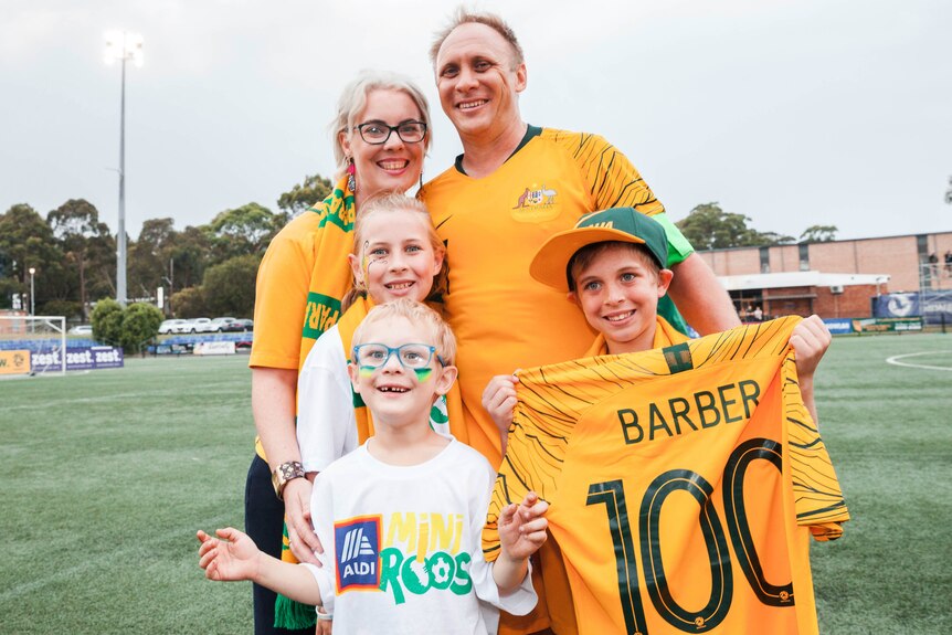 A woman and man with three children wearing yellow soccer jerseys smile as they embrace.