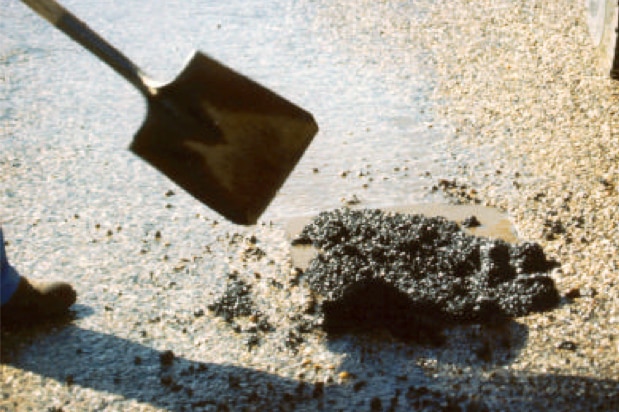 Pothole being fixed with bitumen and shovel.