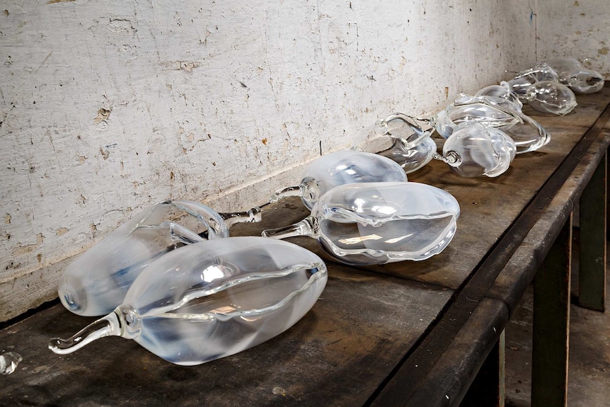 Old and rustly workbench laid with translucent glass forms the shape and size of watermelons, each one cut open.