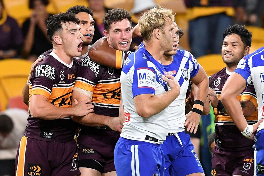 A number of Broncos players converge in celebration as a Bulldogs player looks disappointed in the foreground