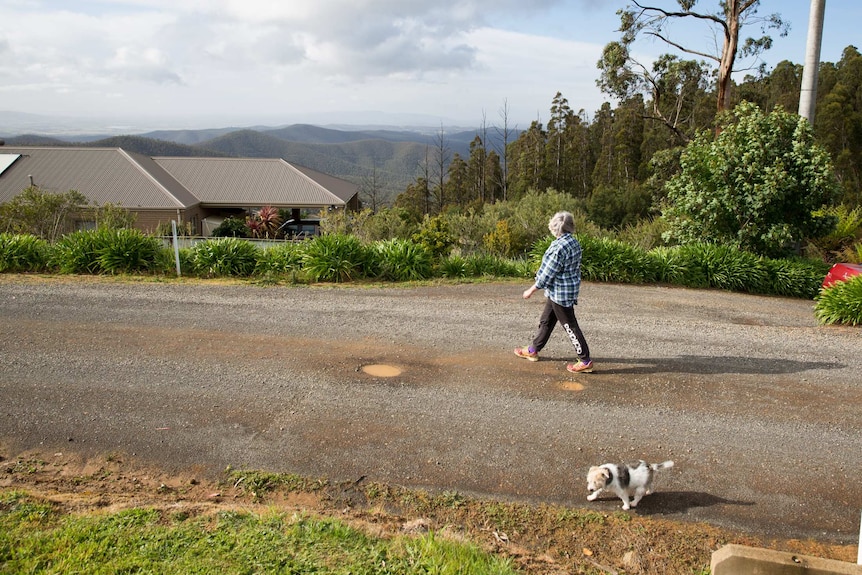 Sandra Molenkamp walks her dog along a road, passing a house, a sweeping view of mountains below.